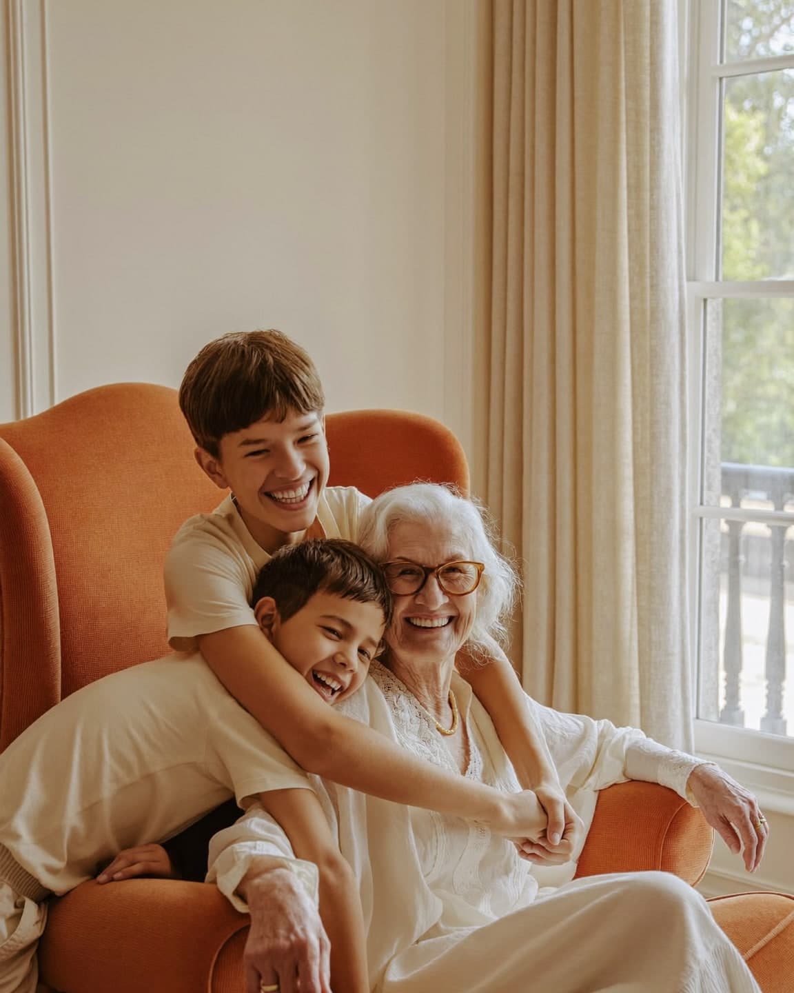 Una abuela ríe en su sillón mientras sus dos nietos la abrazan, en el salón de su casa.